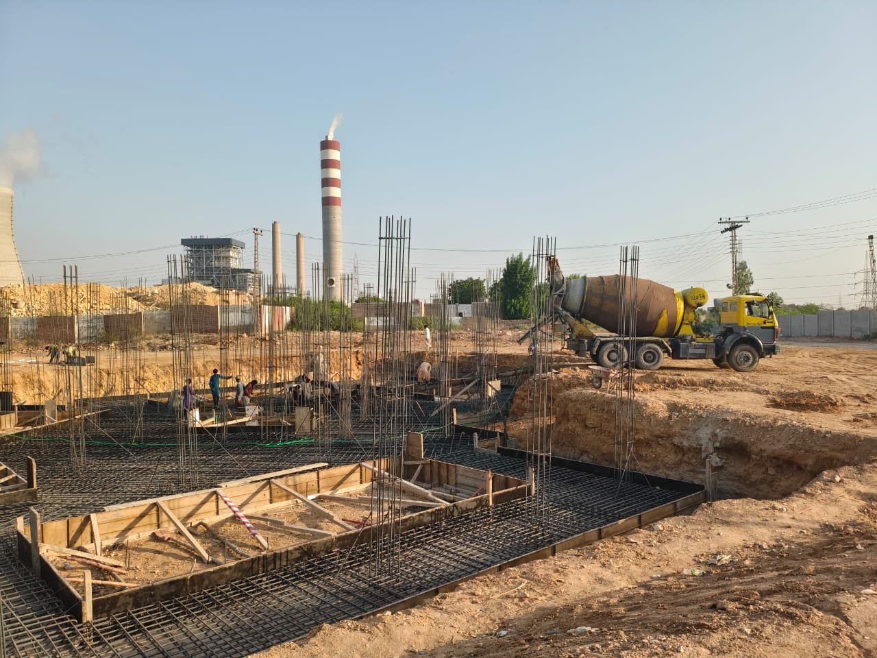 Jamshoro TSG building: concrete mixer and site crew positioned for the bed pour, with reinforcement and formwork in place.